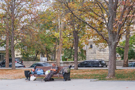 Sevastopol, Russia - September 25, 2020: Two homeless middle-aged men are resting, sleeping on a bench in an autumn city park.のeditorial素材