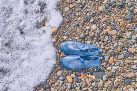Rubber blue women's slippers for swimming on a pebble beach with sea foapの写真素材