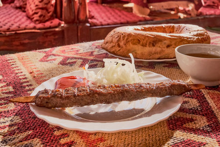 Lamb lula kebab with tomato sauce and pickled onions on a white plate. On the table is a tablecloth with a red asian pattern.の写真素材