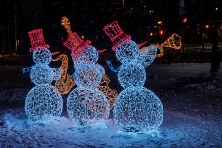 Three colorful glowing snowmen made of wire and garlands play jazz on a winter night city street.のeditorial素材