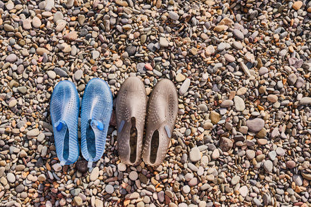 Rubber blue womens and grey mens slippers for swimming on a pebble beach