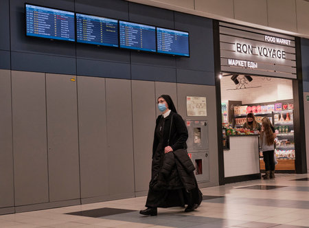 A middle-aged woman, a nun in dark clothes, a white collar and a protective mask walks through the terminal buildingのeditorial素材
