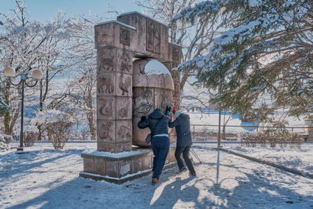 A man and a woman in casual warm clothes turn the egg of desires. The resort park in the winter. Stone sculpture sundial Zodiac signsのeditorial素材