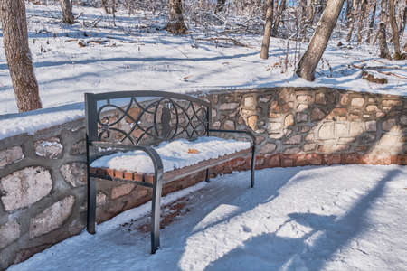Winter landscape. Beautiful melted snow covered bench with openwork patterns and silhouette of Pushkin's head in the Zheleznovodsk Park, Russia.の写真素材