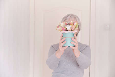 A faceless portrait of an elderly Caucasian woman with short gray hair holding a bouquet of dried flowers. Selective focus on the bouquet.の写真素材