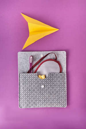 Yellow paper plane and travel kit for comfortable flying on board an airplane on a colored background. Sleep mask, earplugs, textile envelope, toothbrush. Flat lay. Top view.の写真素材