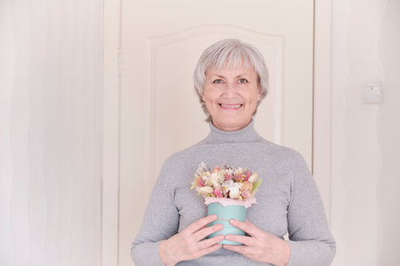 A portrait of a smiling elderly Caucasian woman with short gray hair holding a bouquet of dried flowers.の写真素材