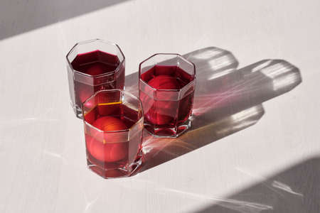 Three eggs in glasses of water is coloring with a natural food dyes of purple, pink, orange colors on a light background with shadows.の写真素材