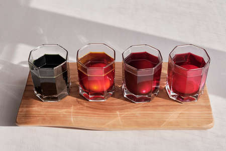 Four eggs in glasses of water in a row on wooden board is coloring with natural dyes in purple, pink, orange, green.の写真素材