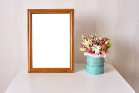 A picture in a wooden frame and a beautiful bouquet of dried flowers on the white table.の写真素材