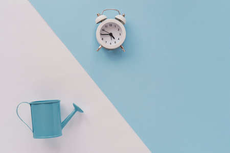 Creative composition Watering time. Toy blue watering can and an alarm clockの写真素材