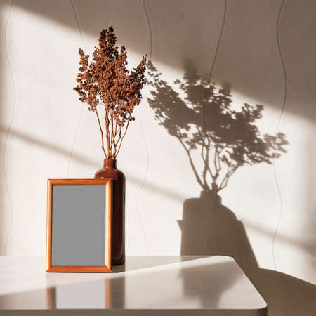 Interior composition. Wooden brown frame mock up, clay vase with brown dried flowers on a white...