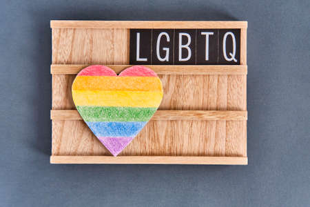 Paper heart painted with colored pencils like a LGBT flag and text LGBTQ on a wooden stand on gray background.の写真素材