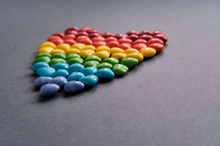 Big heart of small colored candy in the form of hearts like a LGBT flag on gray background.の写真素材