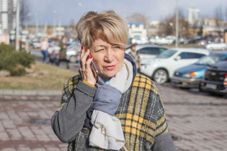 A cute older woman in casual clothes is talking on the phone on a city street in the spring.の写真素材