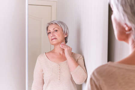 A elderly Caucasian women with short gray hair in casual clothes cares for the skin of face and neckの写真素材
