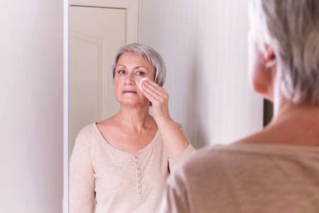 A elderly Caucasian women with short gray hair in casual clothes cares for the skin of the face.の写真素材