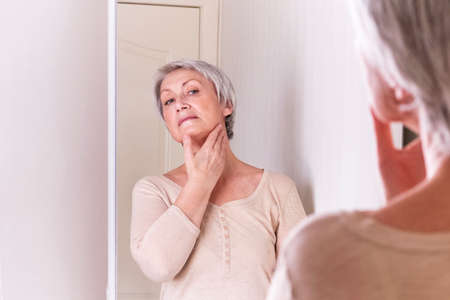 A elderly Caucasian women with short gray hair in casual clothes cares for the skin of the neck, makes self-massageの写真素材