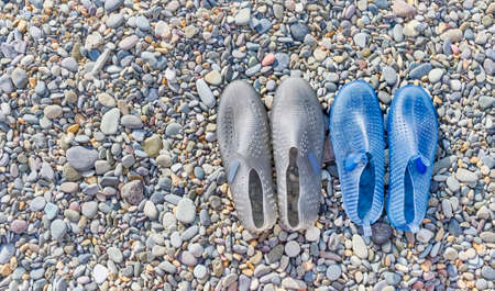 Rubber blue womens and grey mens slippers for swimming on a pebble beachの写真素材