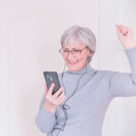 A gray-haired senior woman looking at the smartphone and having joy. Lifestyle moment.の写真素材