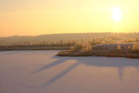 Winter sunset in nature. The snow-covered surface of the lake, trees and bushes.の写真素材