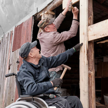 Senior man in a wheelchair in the yard of his house with his friendの写真素材