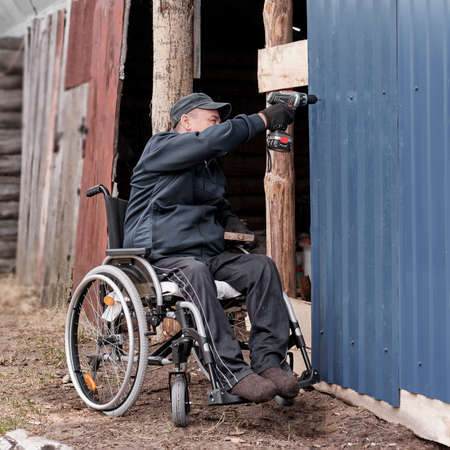 Senior man in a wheelchair in the yard of his houseの写真素材