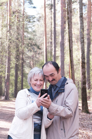 Elderly interracial couple park looking together at a mobile phone screenの写真素材