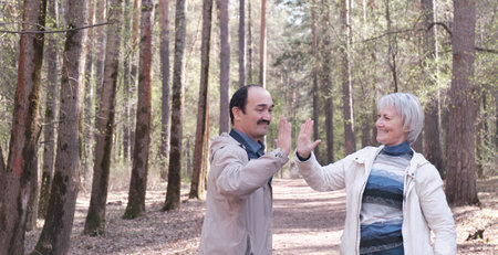 Elderly interracial couple in casual clothes in a spring forest park, facing each other, clap each others hands.の写真素材