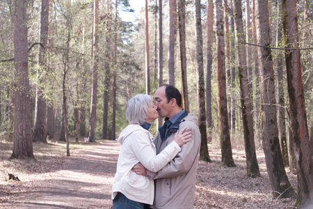 Elderly interracial couple hugging in a spring forest park. A woman kissing a man on the cheek.の写真素材