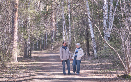 Elderly interracial couple walking in a spring forest park holding hands.の写真素材