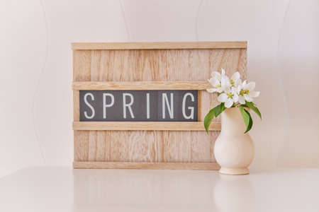 A beautiful a sprig of apple tree with white flowers in a wood vase on the table over the background of the board with the inscription Spring.の写真素材