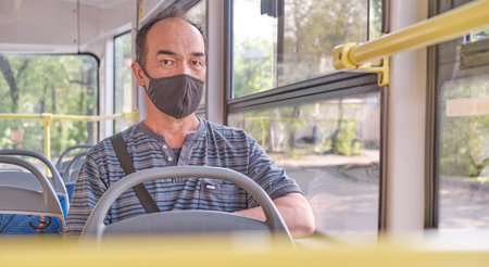 Portrait of senior Asian man wearing a black protective face mask looking at camera in public transport.の写真素材