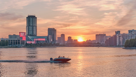 Urban summer landscape. Beautiful sunset on the Iset river. The motor boat goes on the water.のeditorial素材