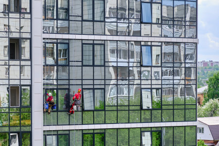 Two industrial climbers from the cleaning service wash the glass facade of a modern high-rise apartment building.のeditorial素材