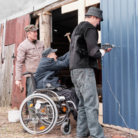 Senior man in a wheelchair in the yard of his house with his friendsの写真素材
