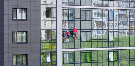 Two industrial climbers from the cleaning service wash the glass facade of a modern high-rise apartment building.のeditorial素材