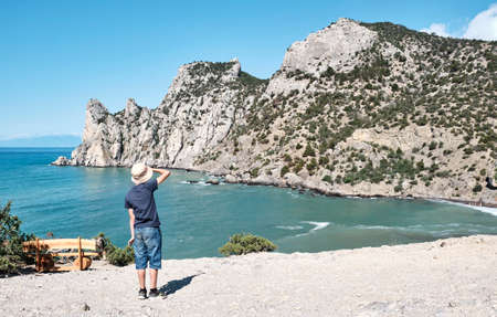 A boy in casual clothes standing on the shore of the bay and looking at the rocks.の写真素材