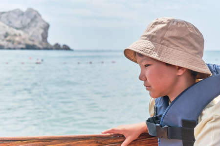 An Asian boy in life jacket floating on pleasure boat on the sea and feeling nauseous.の写真素材