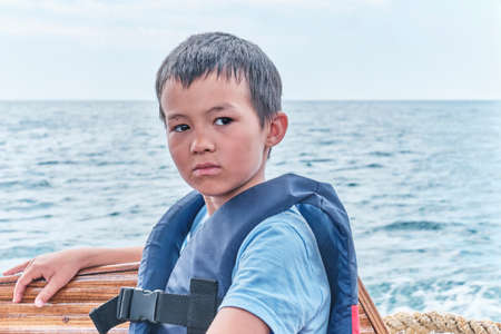 Serious Asian boy in life jacket floating on pleasure boat on the sea.の写真素材