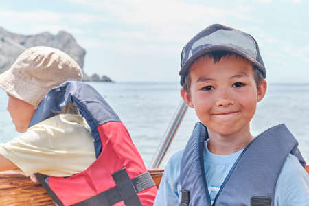 An Asian boy in life jacket floating on pleasure boat on the sea