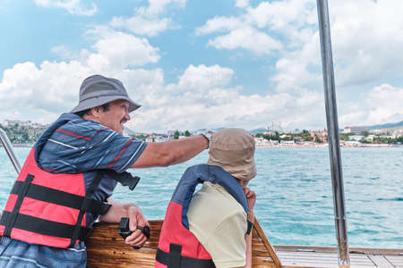 Asian boy and older man, his grandfather, trip on pleasure boat on sea.の写真素材