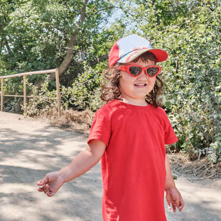 Portrait of a little Asian girl in a red dress, red sunglasses and a baseball capの写真素材