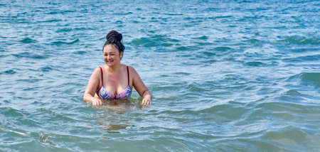 A happy young asian woman in a swimsuit, walking into the sea and smiling.の写真素材