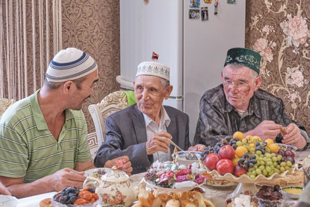 Local residents of Siberian village celebrate Muslim holiday Kurban Bayram at their home table. Mullah talking with villagers. Eid al-Adhaのeditorial素材