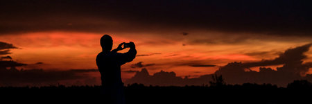 Silhouette of man taking pictures on mobile phone beautiful dramatic sunset.の写真素材