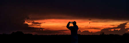Silhouette of man taking pictures on mobile phone beautiful dramatic sunset.の写真素材