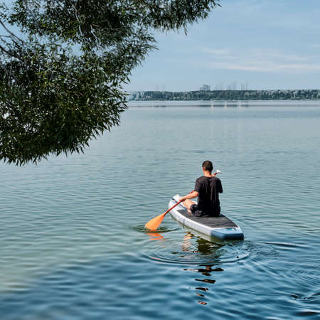 Asian older man on sup board on calm lake.の写真素材