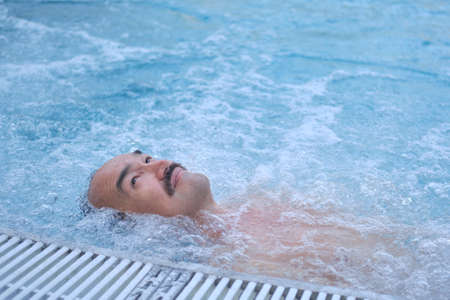 Happy mature asian man laying on water relax in outdoor thermal pool with hydromassage.の写真素材