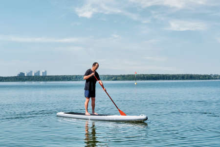 Asian older man on sup board on calm lake.の写真素材